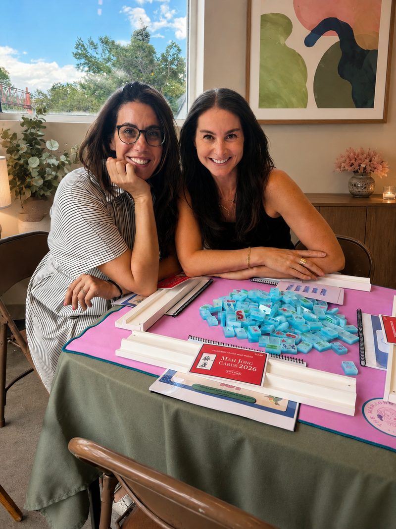 Alex and Erica smiling at a table set with mahjong tiles, racks, and cards